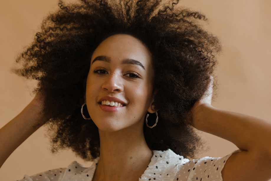 Cheerful young black lady touching Afro hair and smiling in studio